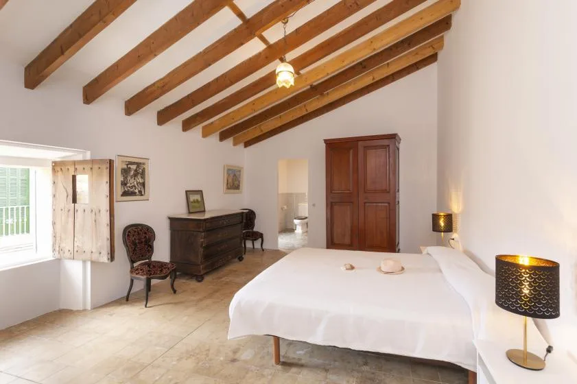 A bright bedroom with a large bed and exposed wooden ceiling beams.