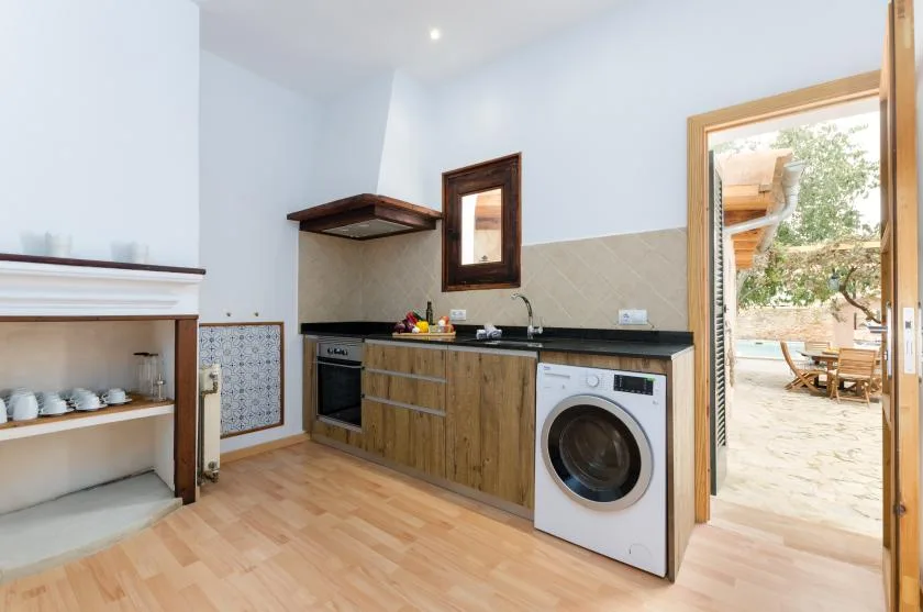 A compact kitchen with wood cabinetry and a washing machine beside an open patio door.