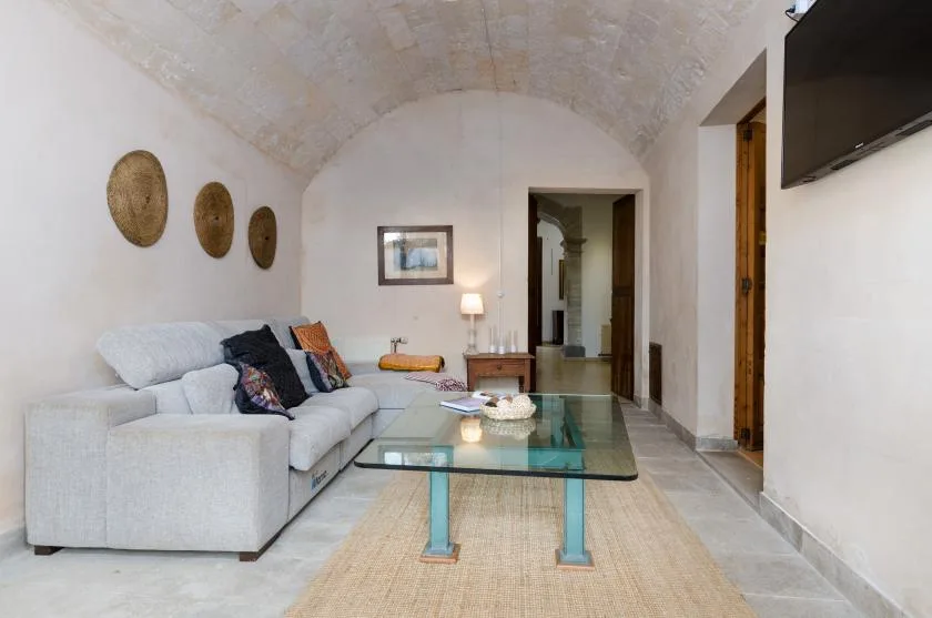 A living room with seating and a glass coffee table beneath a vaulted ceiling.