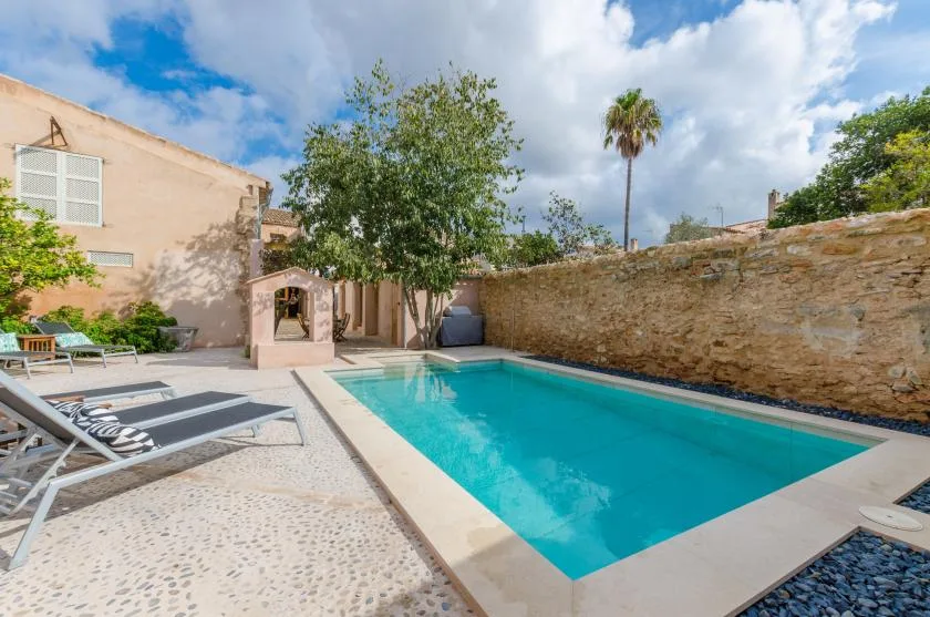 An outdoor swimming pool sits beside a paved patio and low stone wall.