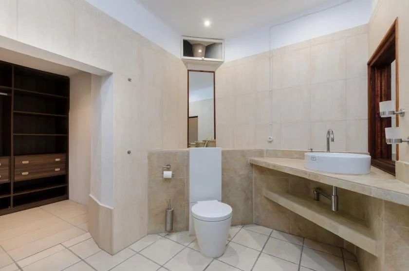 A tiled bathroom with a toilet, sink, and open shelving.
