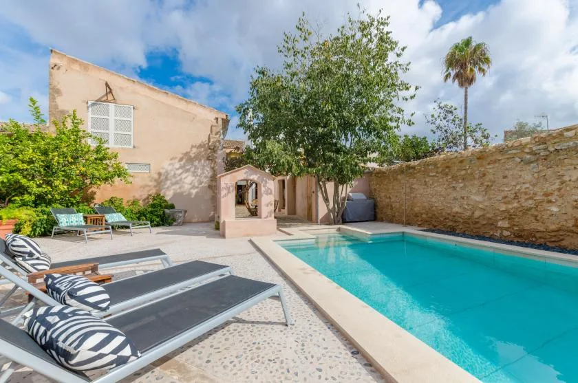 A courtyard pool beside a pale building, with lounge seating and leafy trees.