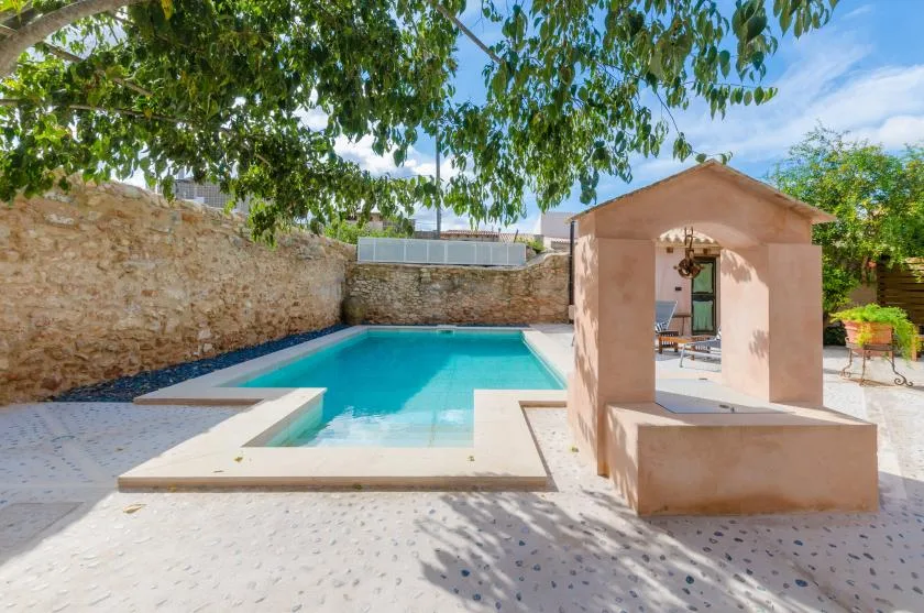 An outdoor swimming pool sits beside a small shaded pavilion.