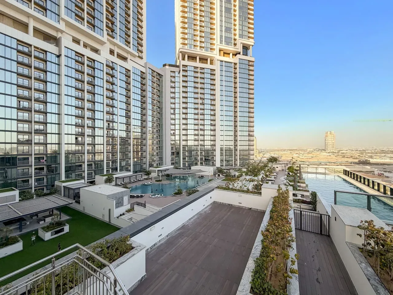 Un complejo residencial de gran altura domina terrazas ajardinadas y una piscina.
