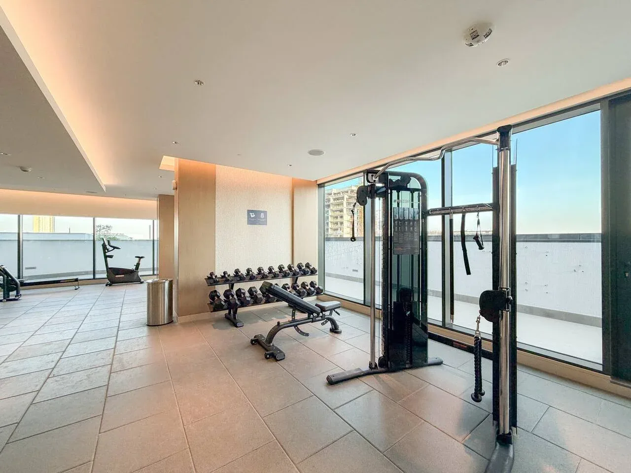 Un gimnasio luminoso con máquinas de ejercicio y grandes ventanas.