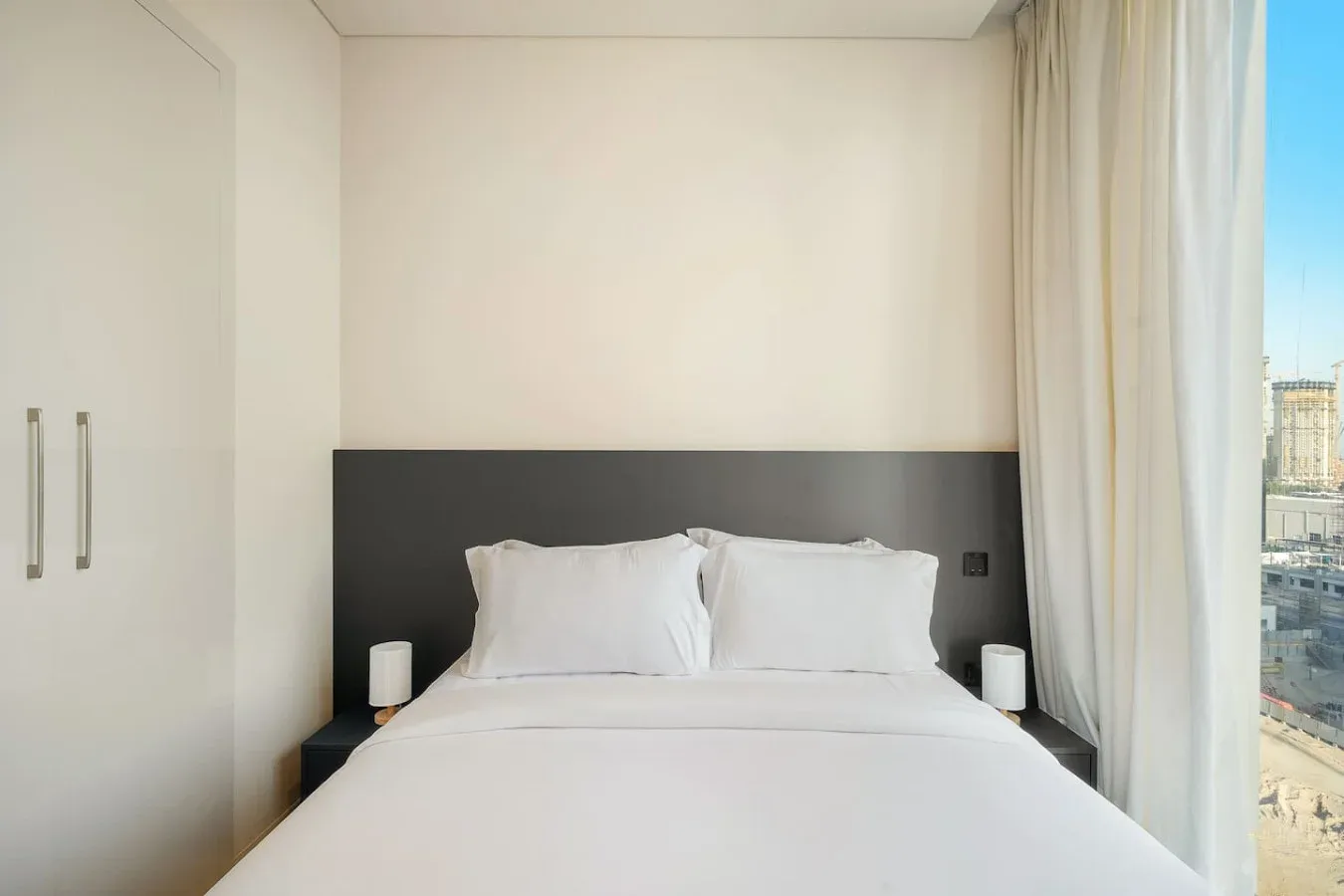 Un dormitorio con una cama bien tendida junto a una ventana alta con cortinas.