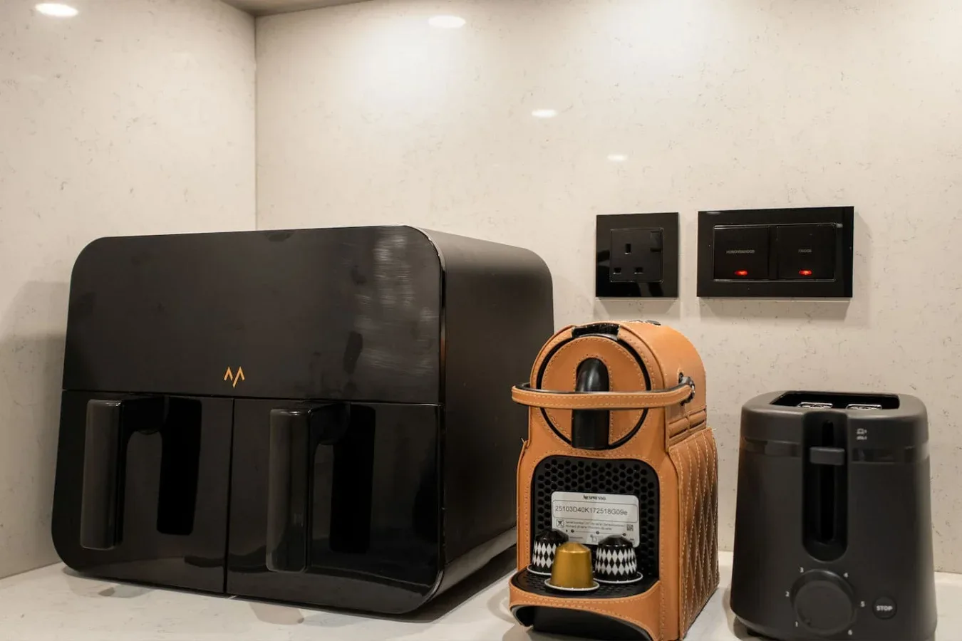 Una encimera de cocina con una cafetera y pequeños electrodomésticos junto a una pared clara.