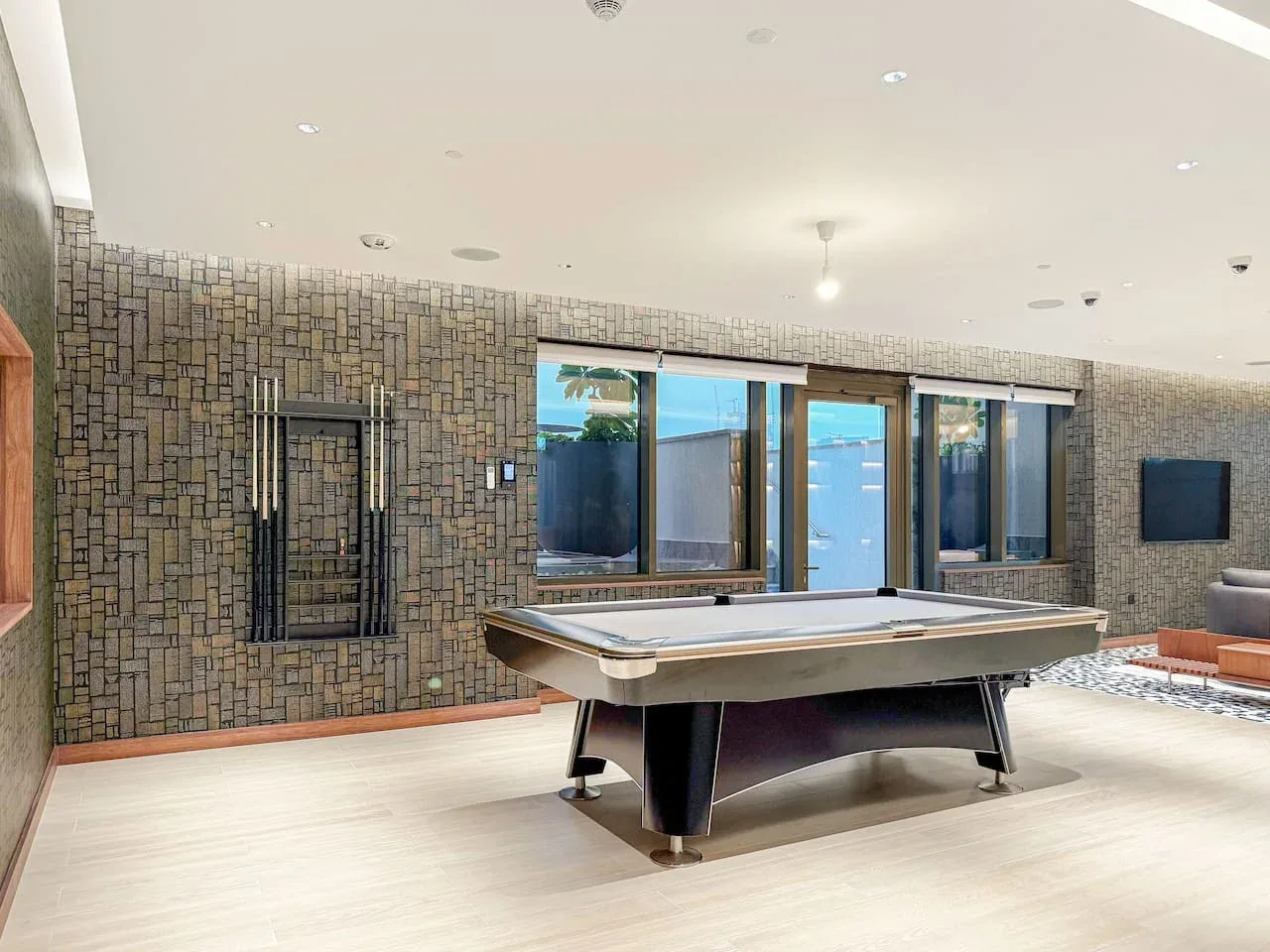Una mesa de billar está en una sala de recreación luminosa con grandes ventanas.