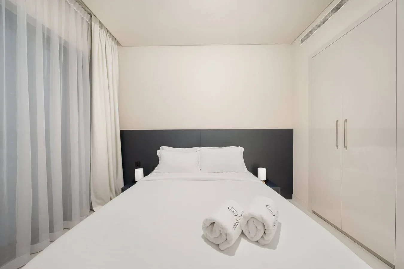 Un dormitorio con una cama tendida y cortinas translúcidas junto a la ventana.