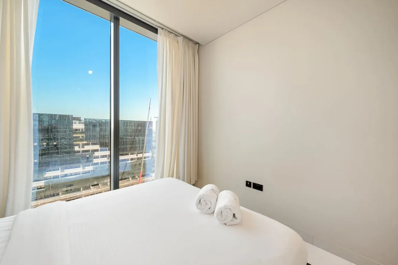 Un dormitorio luminoso con una cama blanca junto a una gran ventana con cortinas.