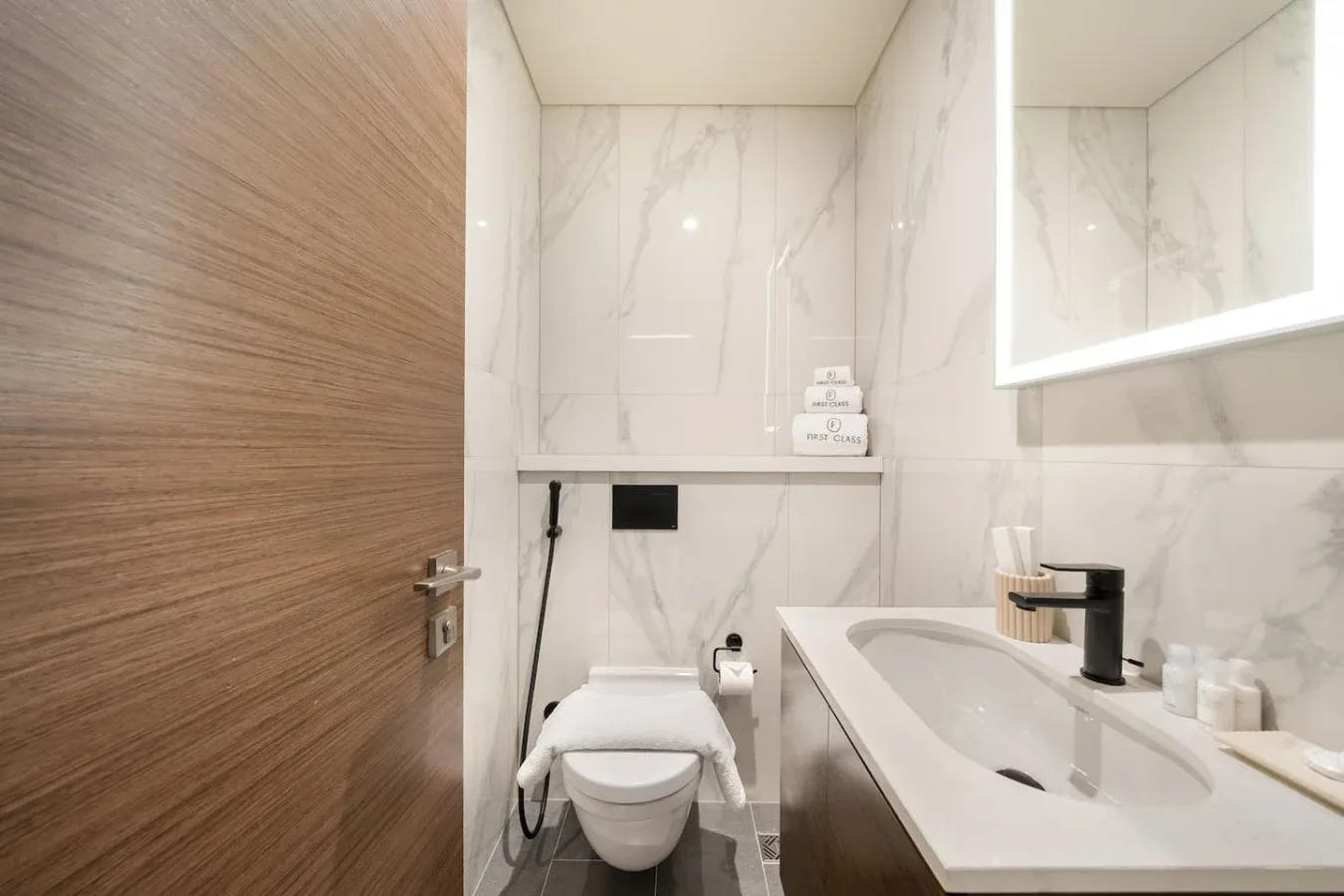 Un baño luminoso con azulejos veteados tiene un inodoro, lavabo y espejo.