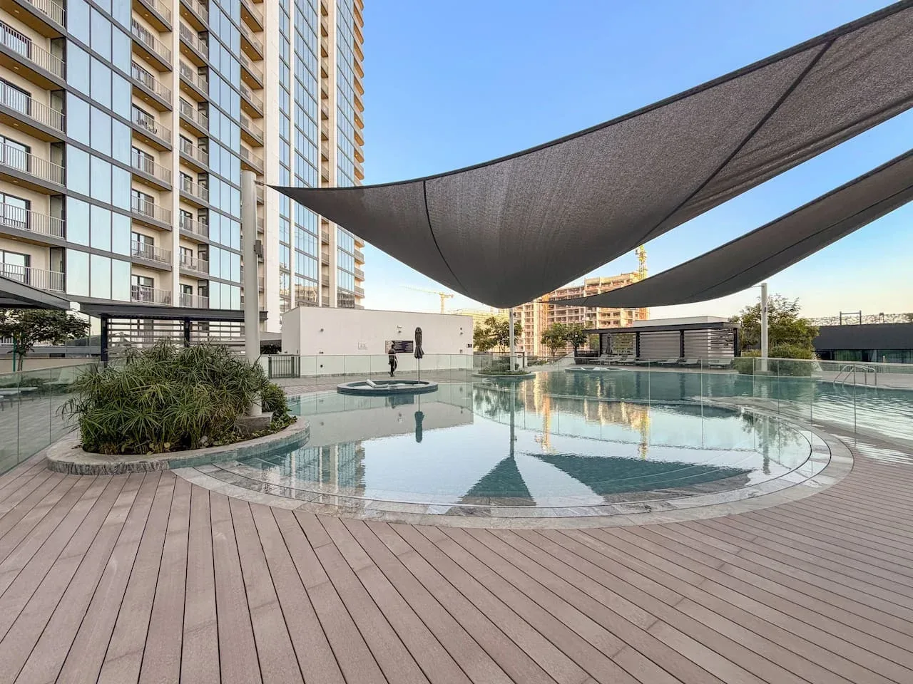 Una piscina al aire libre está bajo grandes toldos junto a un edificio alto.