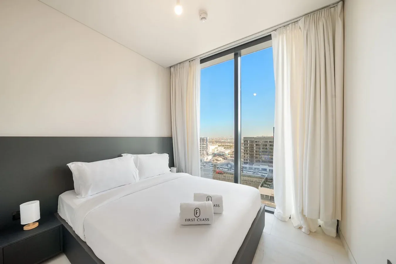 Un dormitorio con una cama bien tendida junto a una gran ventana con cortinas.