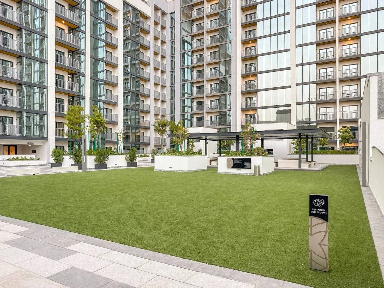 Un patio ajardinado con un amplio césped y edificios de apartamentos modernos.
