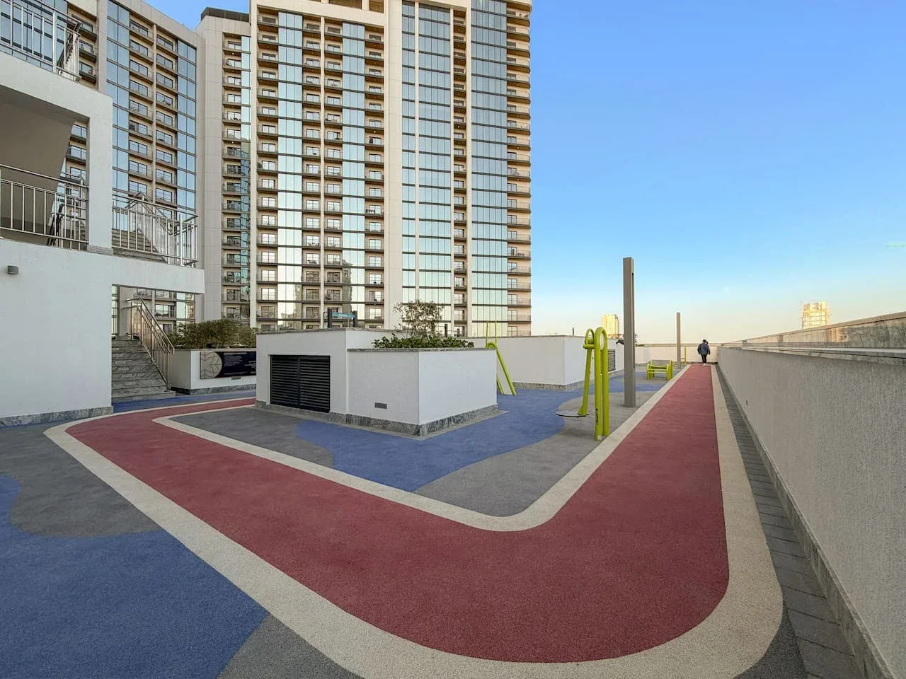 Una zona recreativa en la azotea tiene una pista roja, equipos de ejercicio y edificios altos.