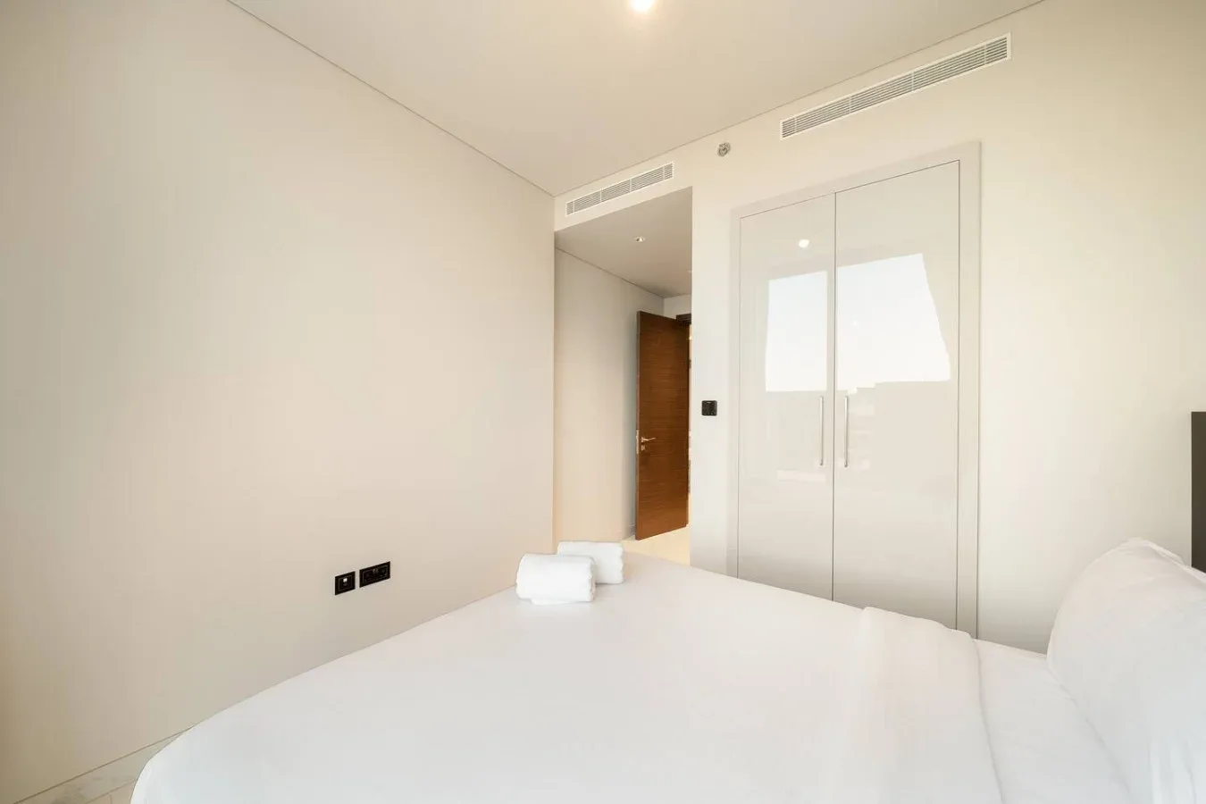 Un dormitorio luminoso con una cama blanca y puertas con paneles de vidrio.