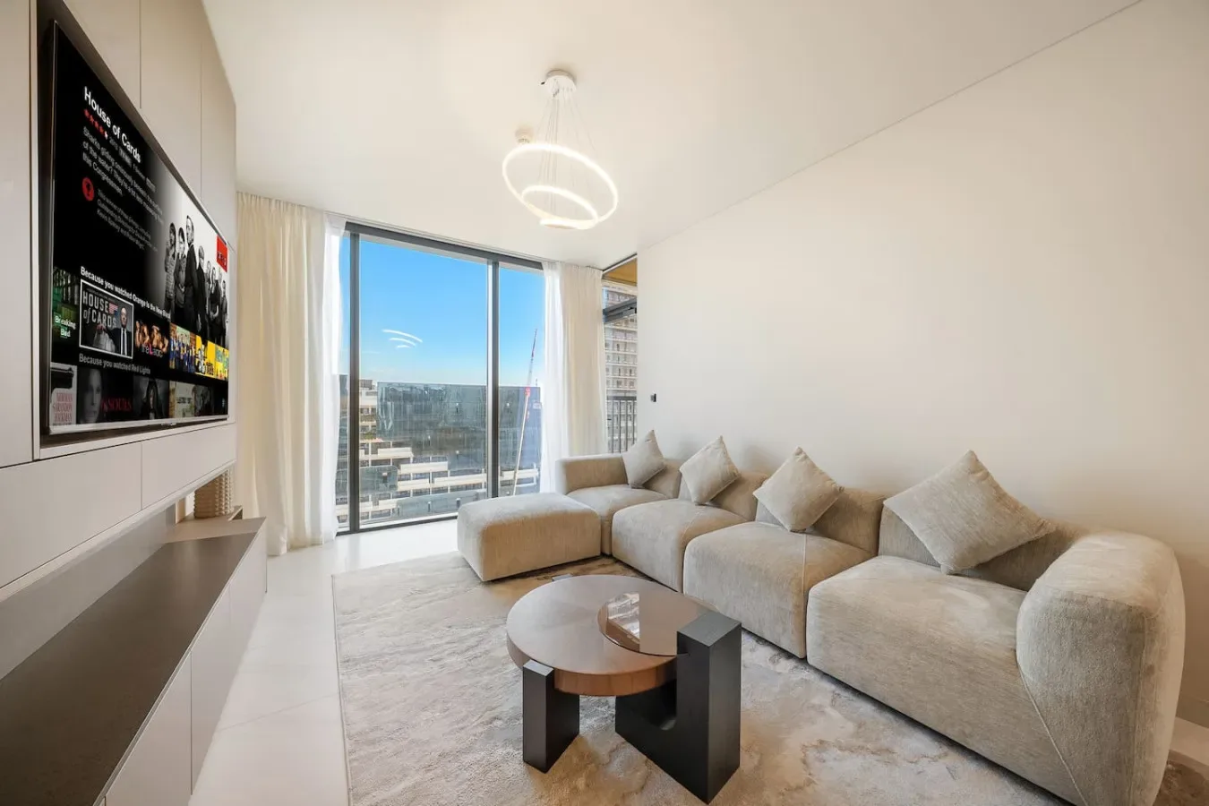 Una sala luminosa con asientos, una mesa de centro y grandes ventanas con vistas a la ciudad.
