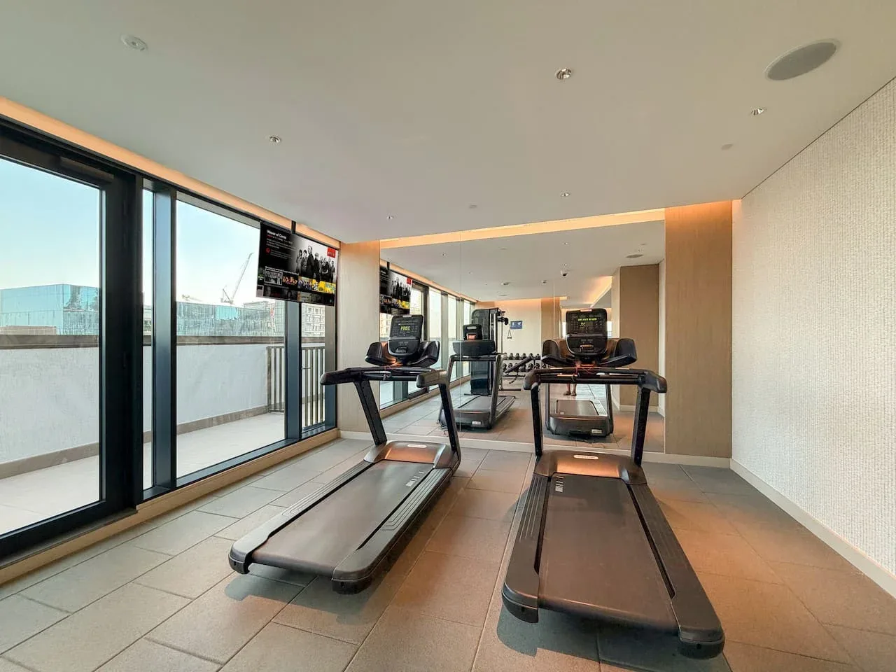 Una sala de ejercicio con cintas de correr junto a grandes ventanales.
