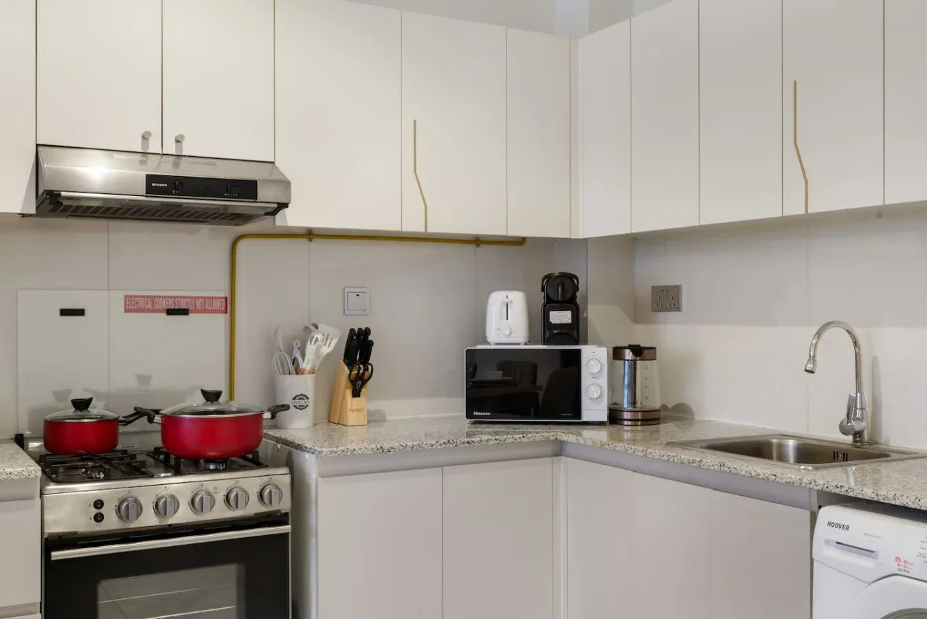 A kitchen with white cabinets, a stove, and appliances on the counter.