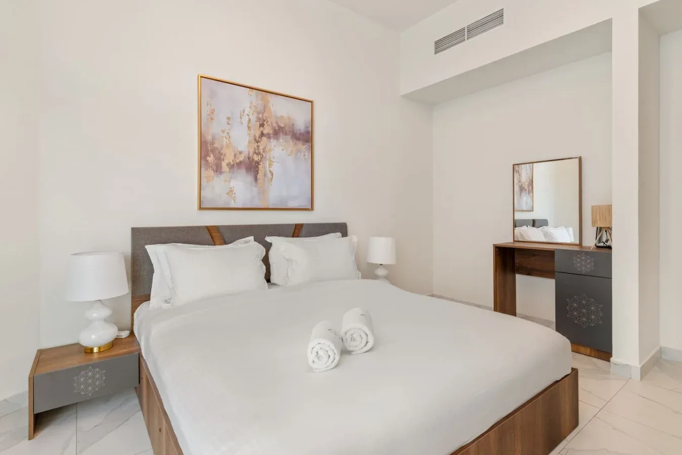 A bedroom with a neatly made bed and abstract artwork above it.