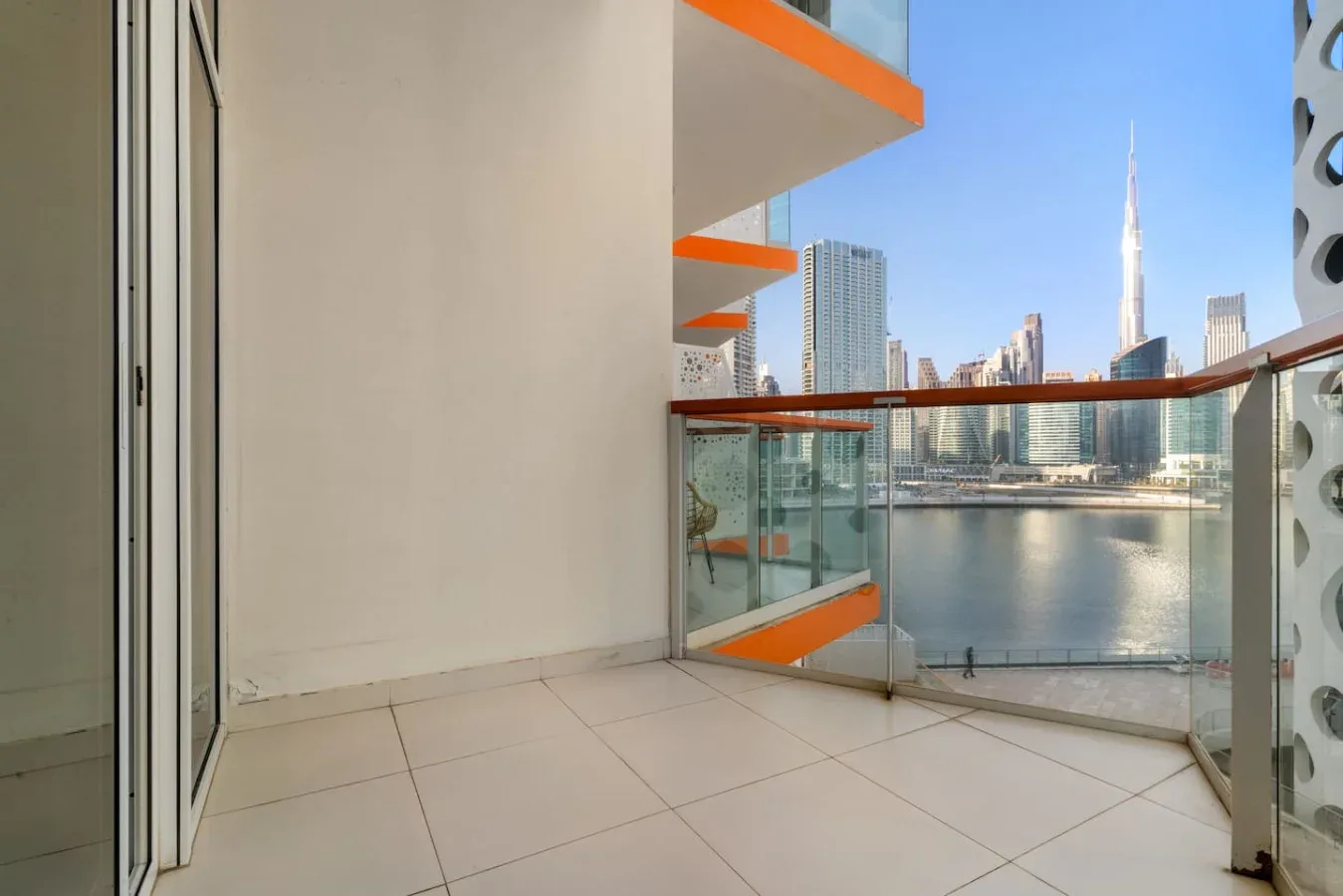 A tiled balcony overlooks a calm body of water and a modern city skyline.
