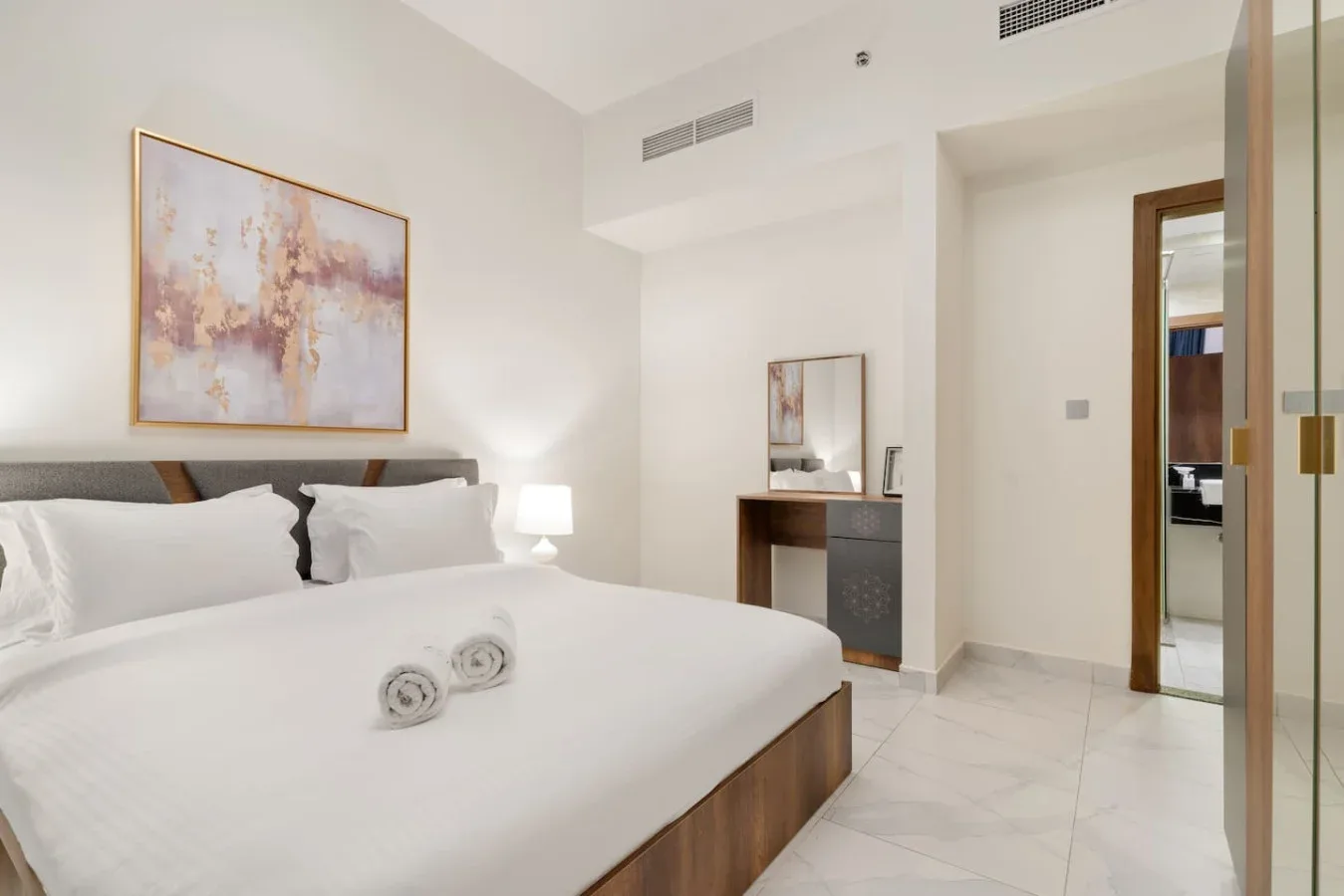 A bright bedroom with a neatly made bed and framed artwork on the wall.