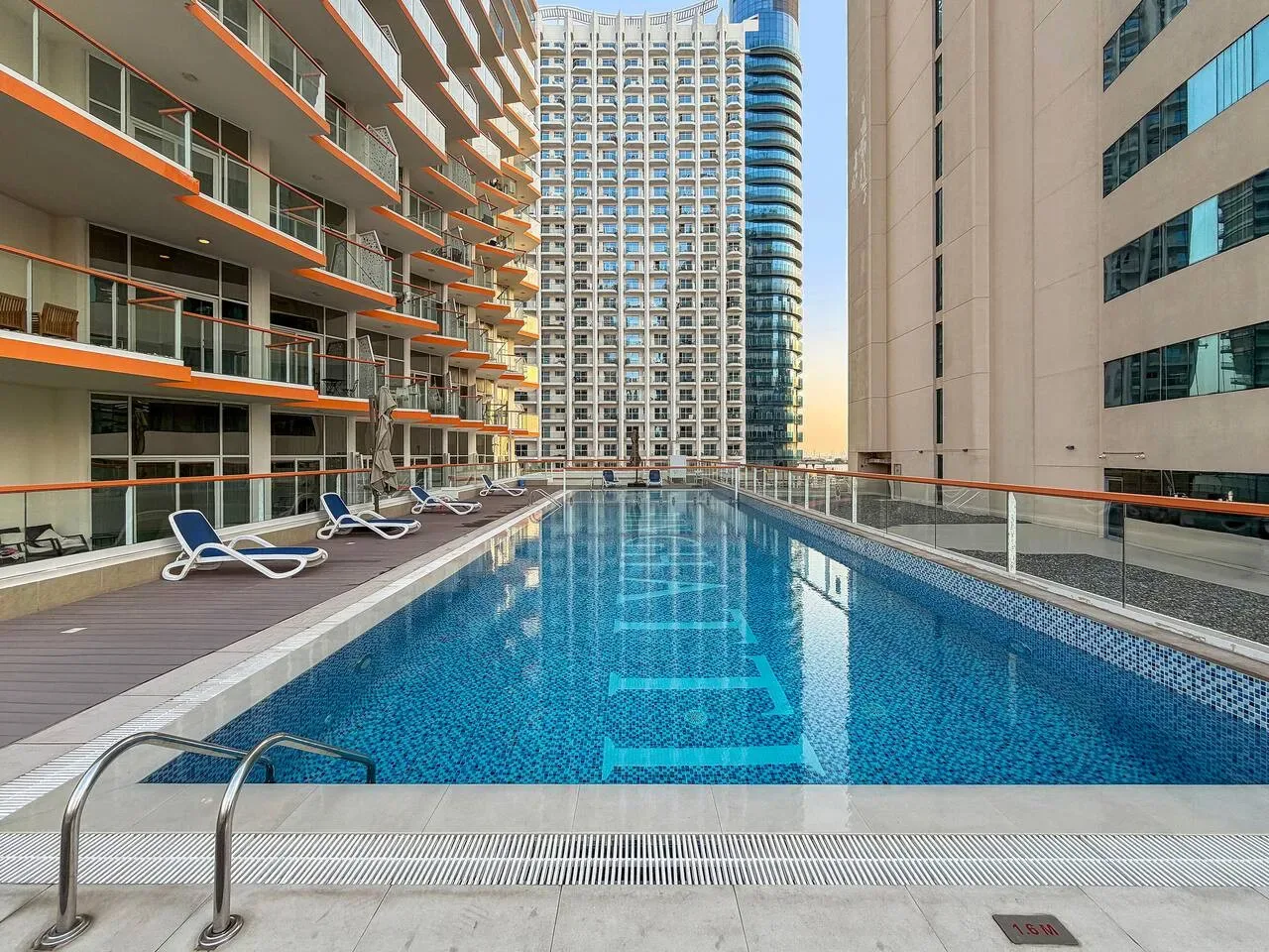 A swimming pool between modern buildings, with lounge chairs along the deck.