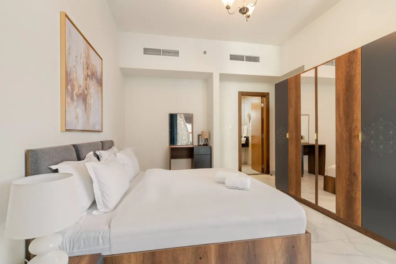 A bright bedroom with a neatly made bed and mirrored wardrobes.