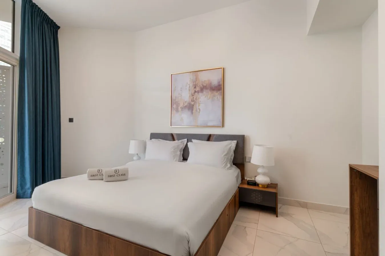 A bedroom with a neatly made bed, bedside tables, and a framed artwork.