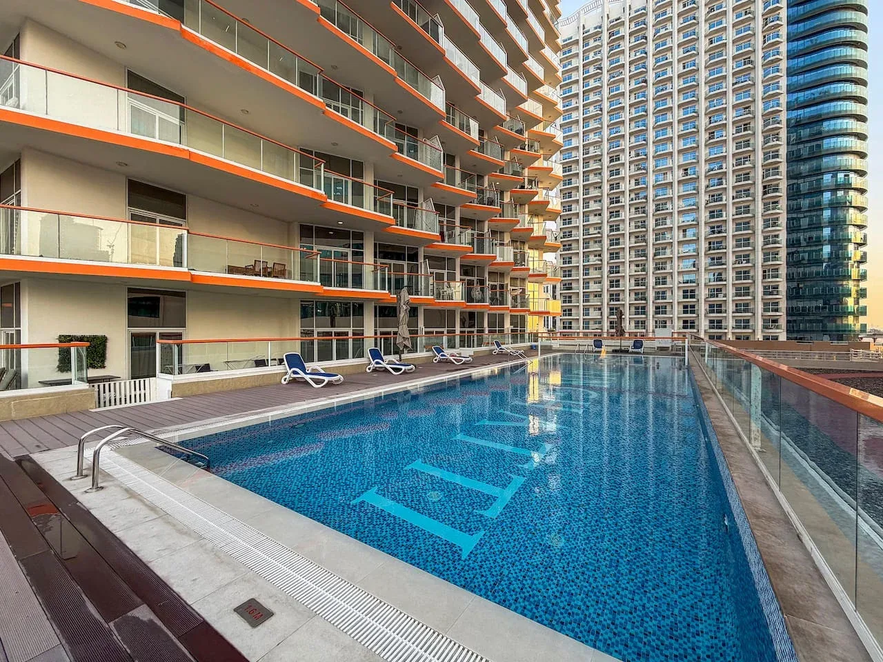 A long outdoor swimming pool sits beside modern high-rise buildings.