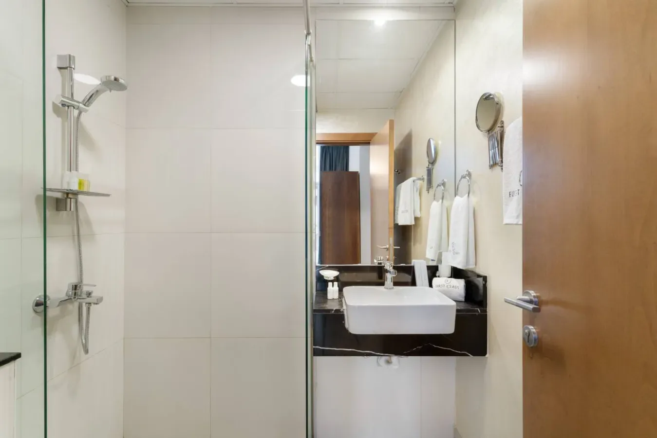 A bathroom with a glass shower and a sink beside the open doorway.