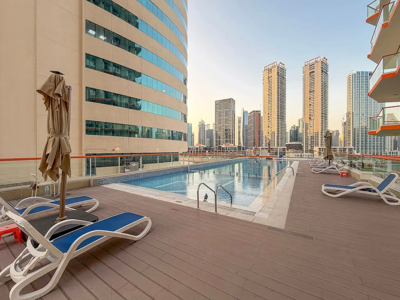 An outdoor swimming pool sits among lounge chairs, with high-rise buildings in the background.