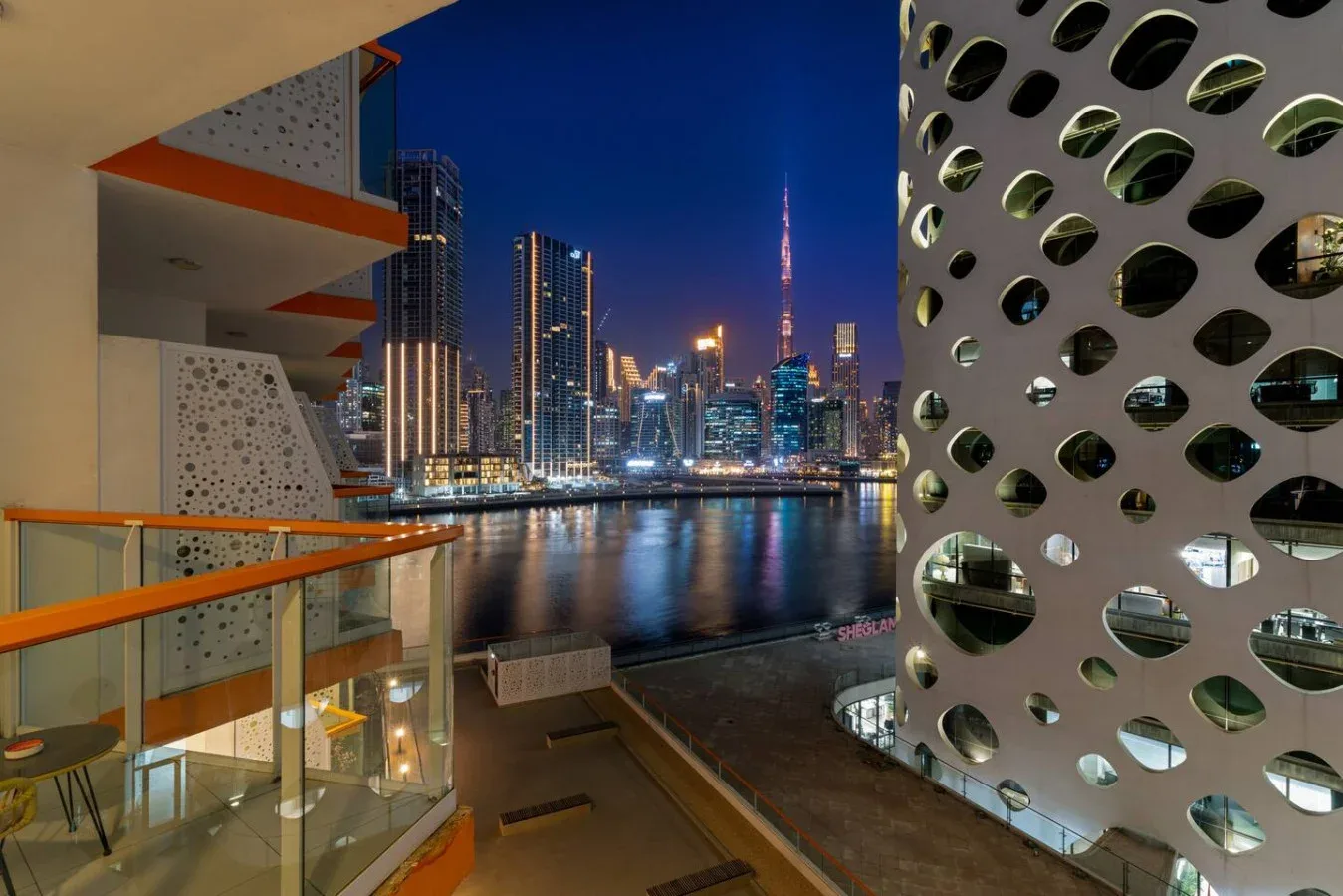 A balcony overlooks a waterfront city skyline illuminated at night.