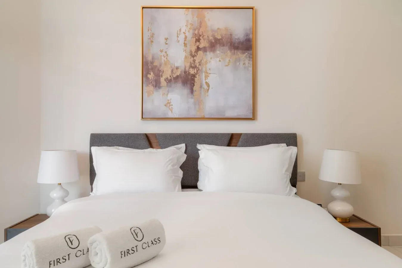 A bedroom with a neatly made bed and abstract artwork above the headboard.