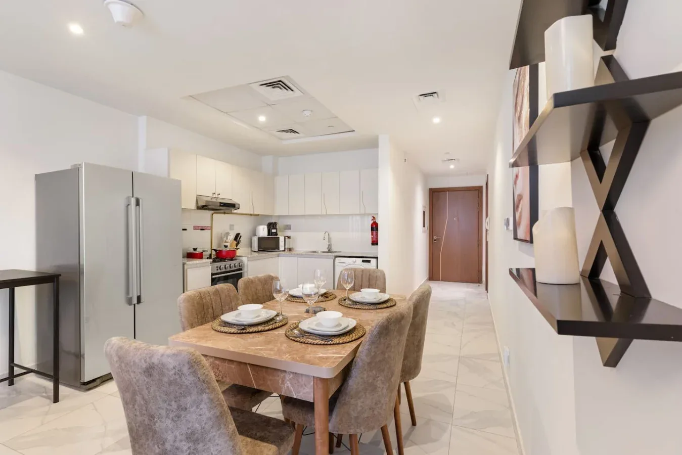 A dining area with a wooden table and upholstered seating beside a kitchen.