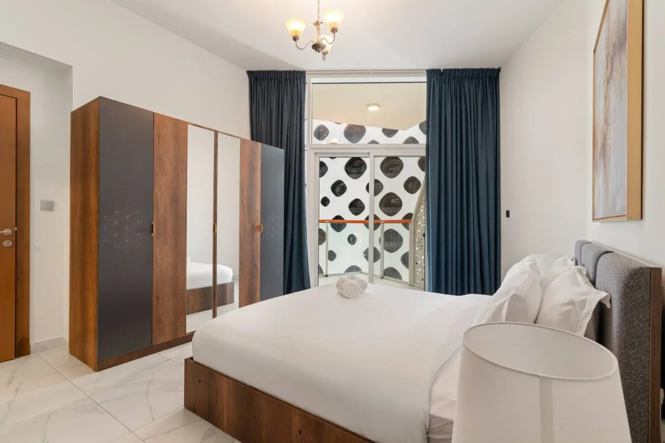 A bright bedroom with a large bed, wardrobes, and dark curtains.