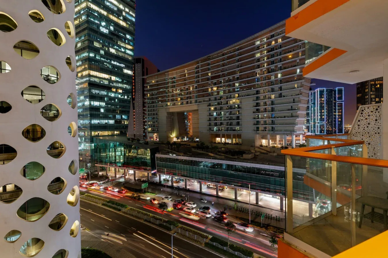 Nighttime city view of illuminated buildings and traffic along a busy street.