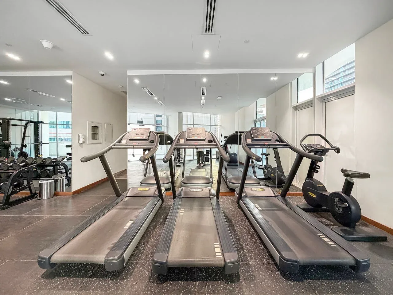 A gym with treadmills and exercise equipment beside mirrored walls.