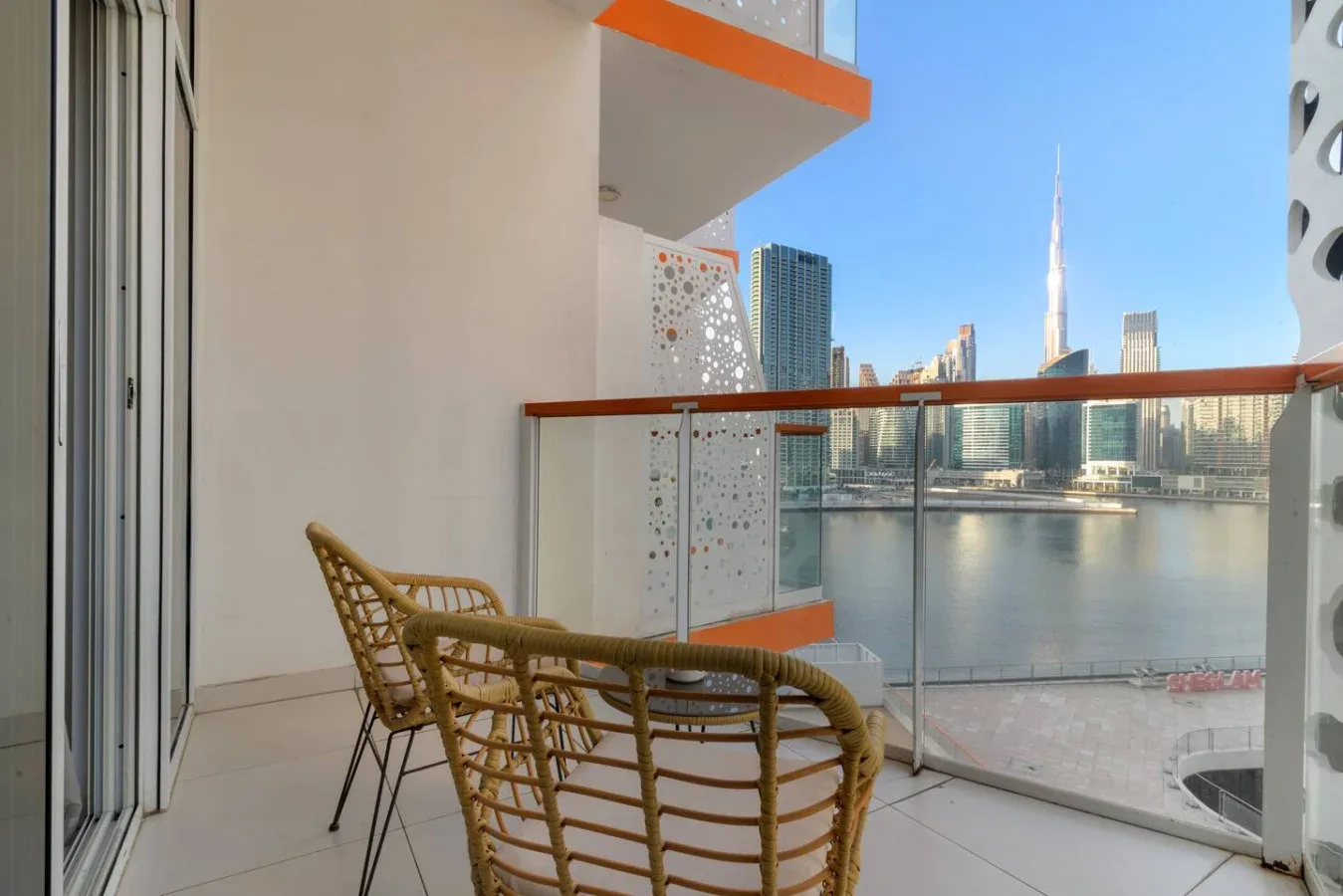 A balcony seating area overlooks the water and a city skyline.