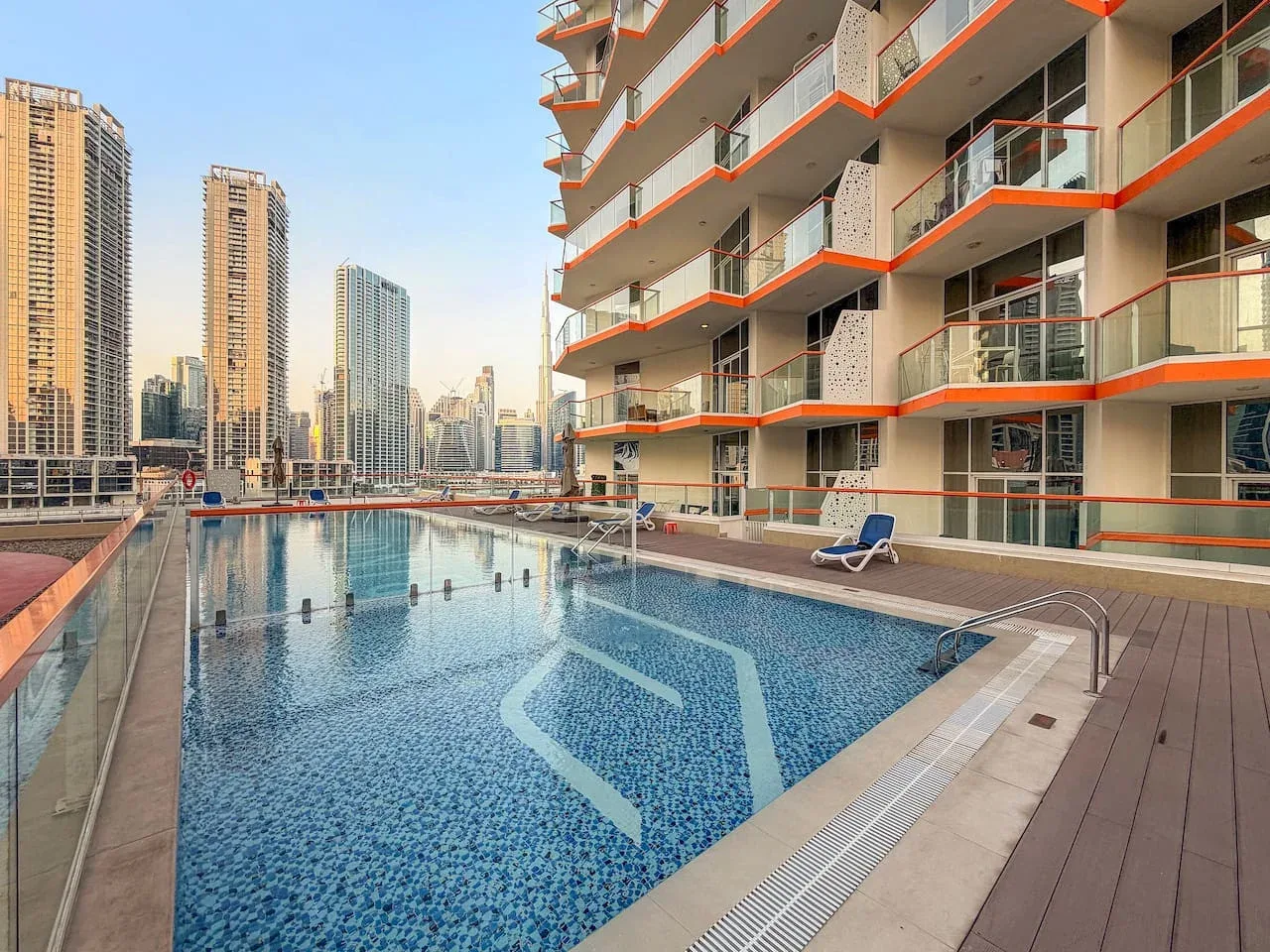 A rooftop swimming pool beside a modern high-rise building, with city towers in the background.