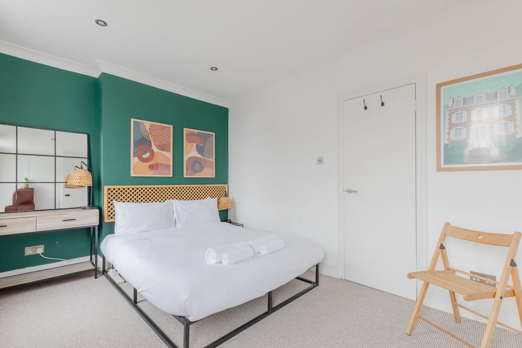 A bedroom with a white bed against a green accent wall.
