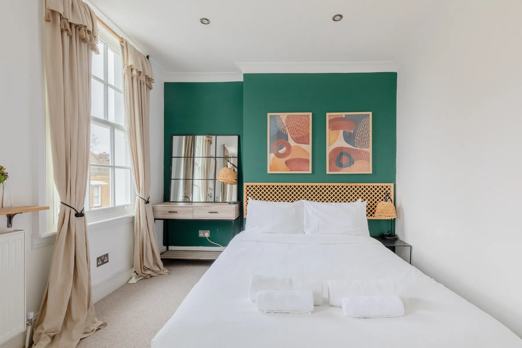 A bright bedroom with a white bed against a green accent wall.