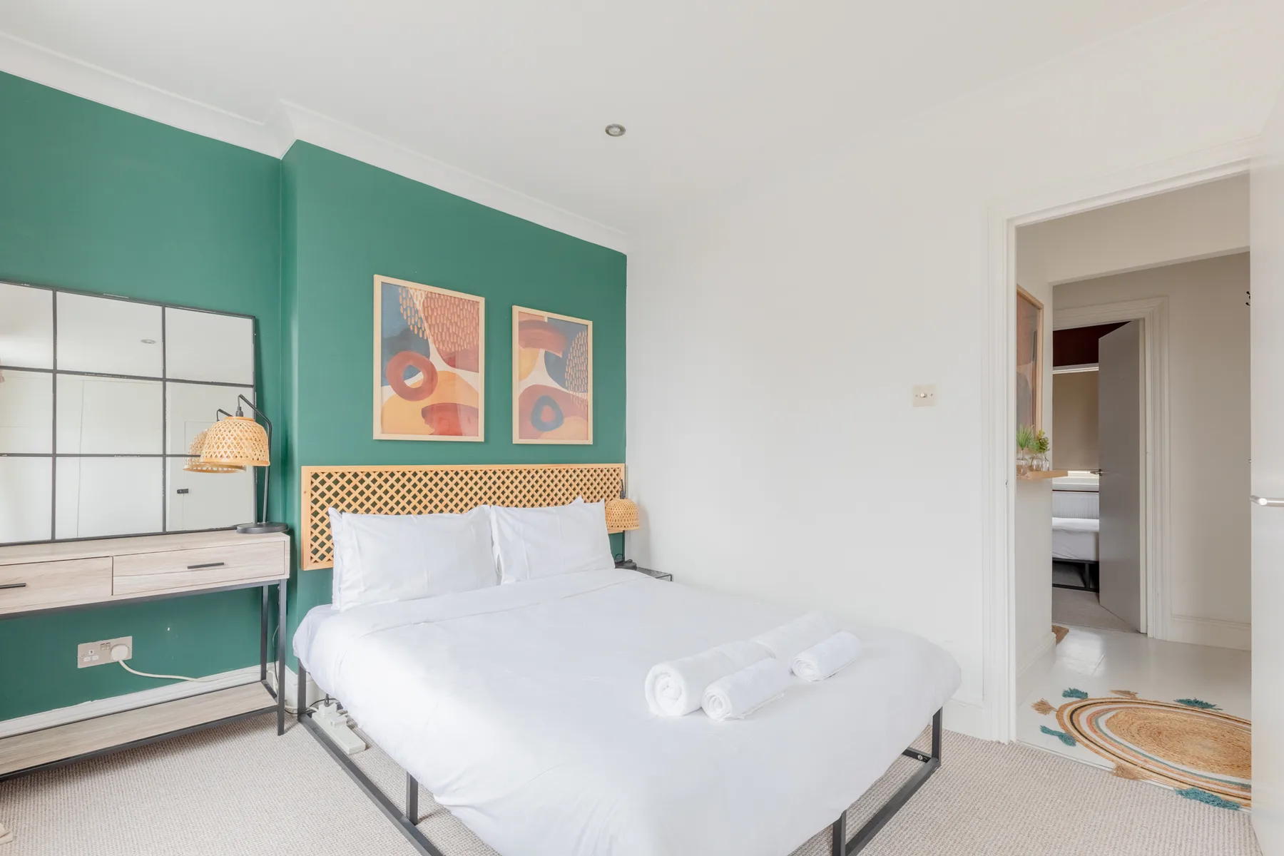 A bedroom with a white bed against a green accent wall.