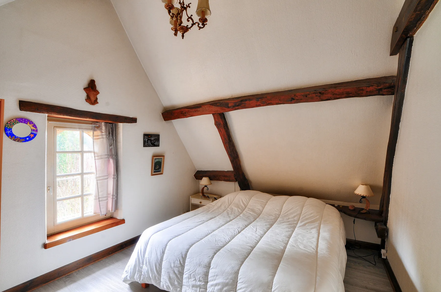Un dormitorio con una cama bajo vigas de madera vistas y un techo inclinado.