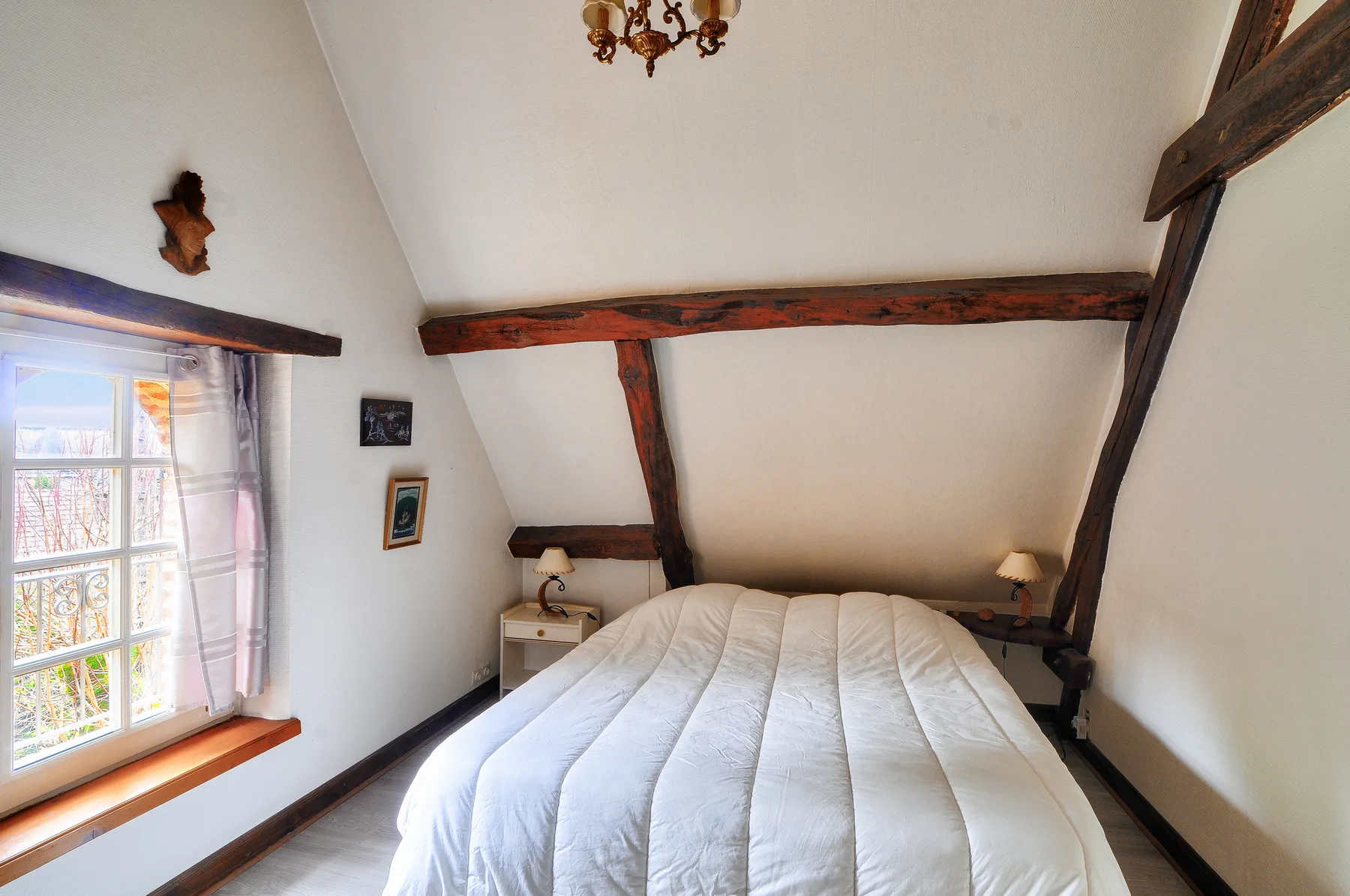 Dormitorio con una cama bajo vigas de madera vistas y una ventana.