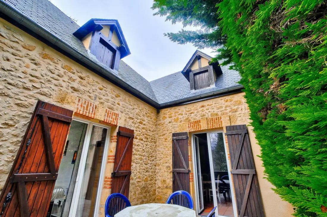 Exterior de una casa de piedra con ventanas con contraventanas y asientos al aire libre.