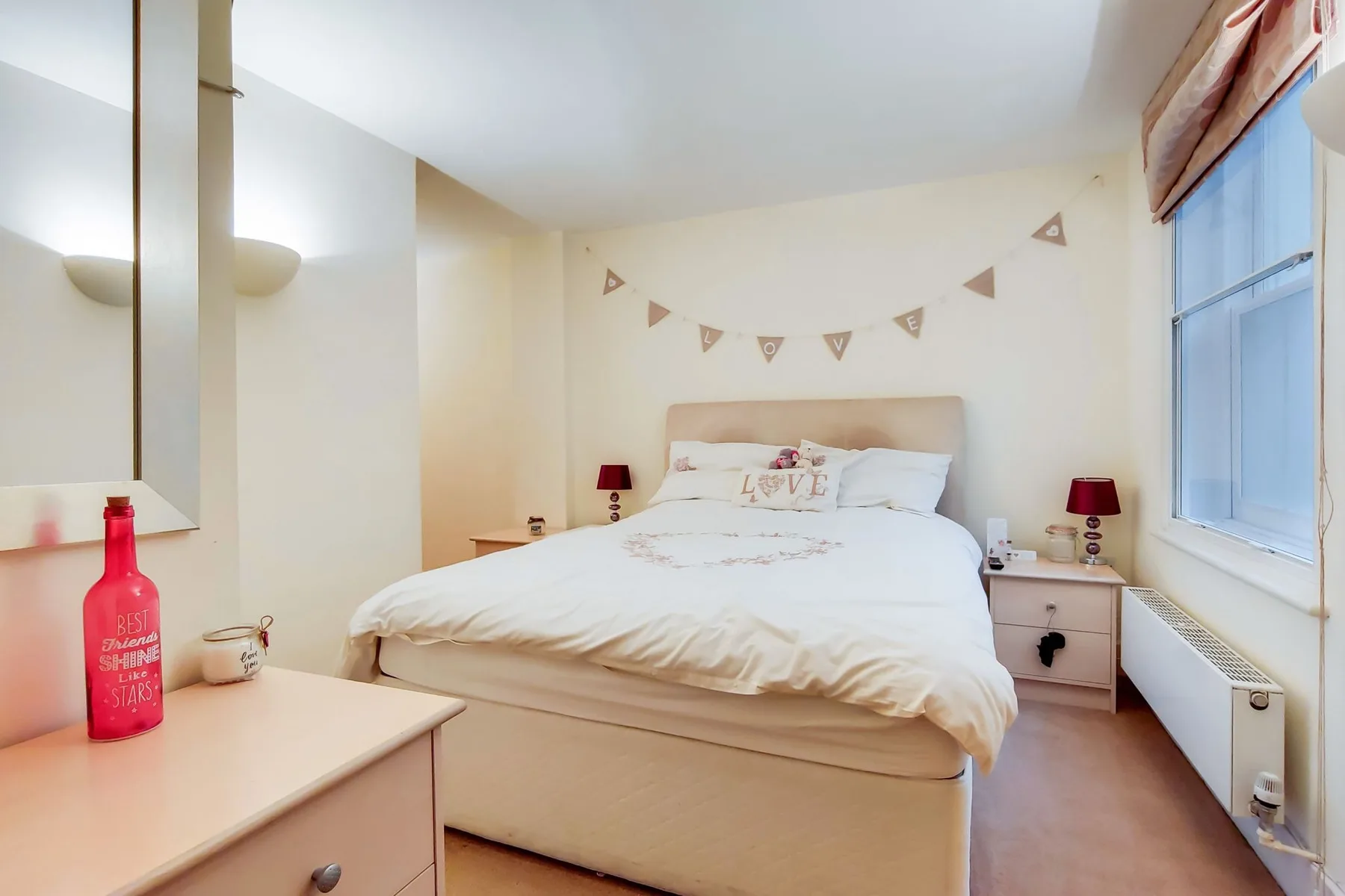A bedroom with a bed, bedside tables, and a window.