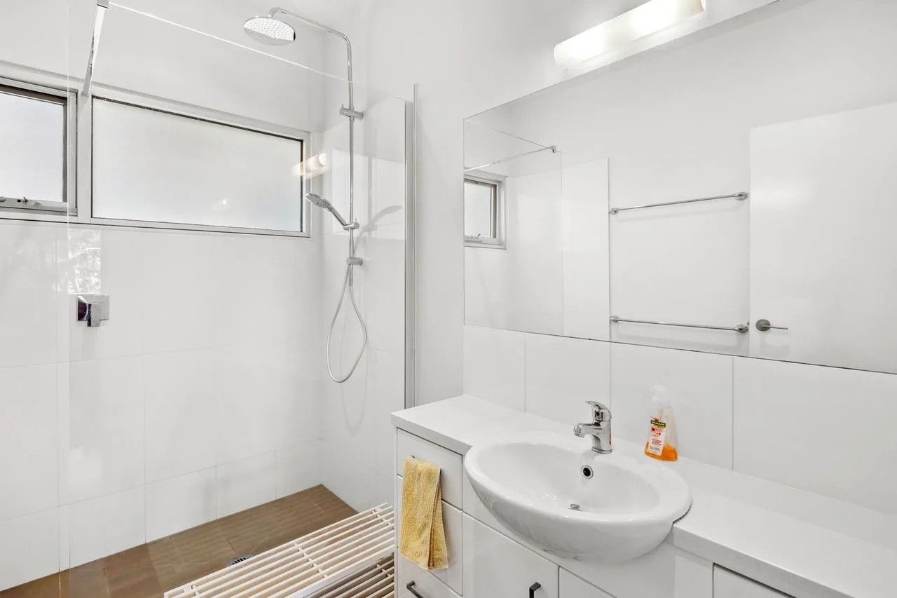 Un baño luminoso con ducha, ventana y lavabo.
