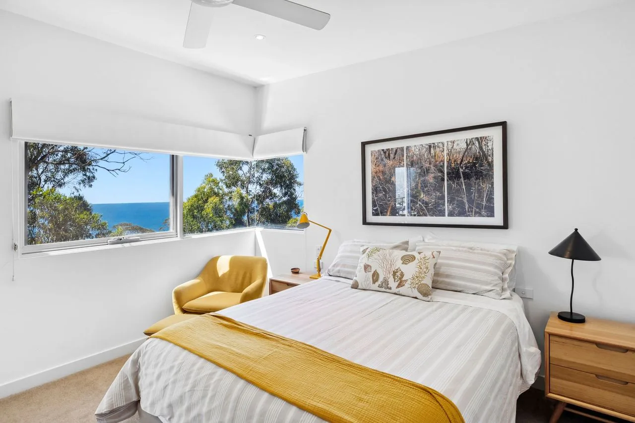 Un dormitorio luminoso con una cama, una manta mostaza y una ventana amplia.