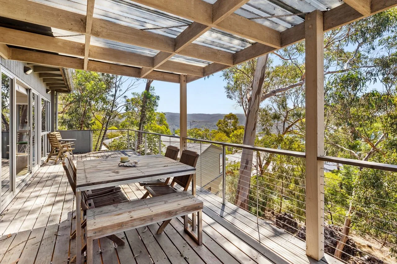 Comedor exterior cubierto con una mesa de madera y árboles alrededor.